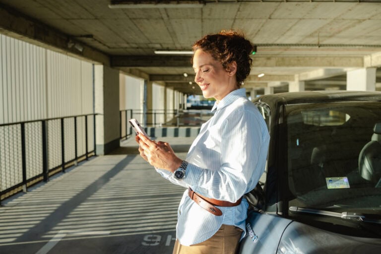 Lysegrå bil i underjordisk parkeringshus med kvinne som bruker mobiltelefon.